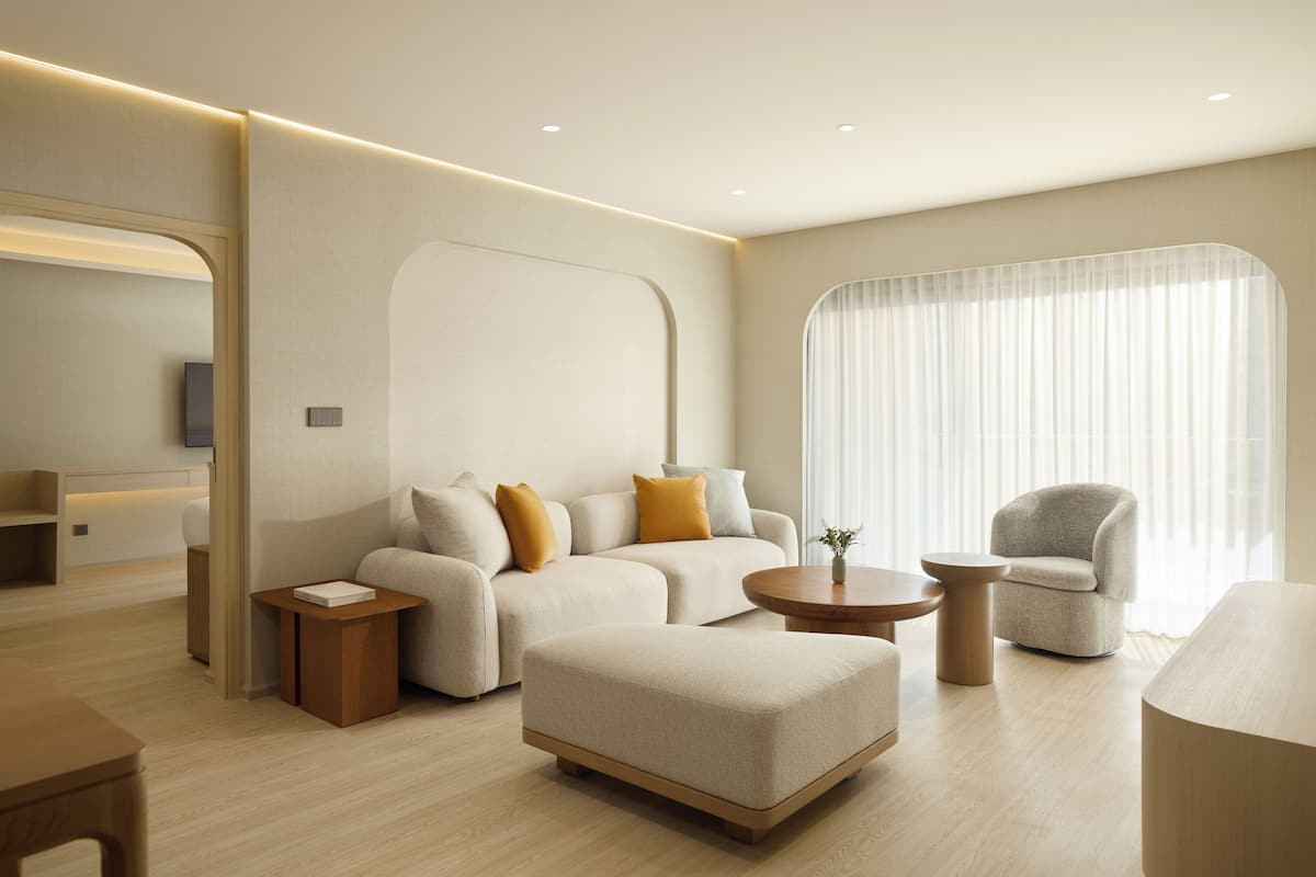 A modern living room with a sofa, ottoman, armchair, and coffee table. There is a television and a small table with a book.