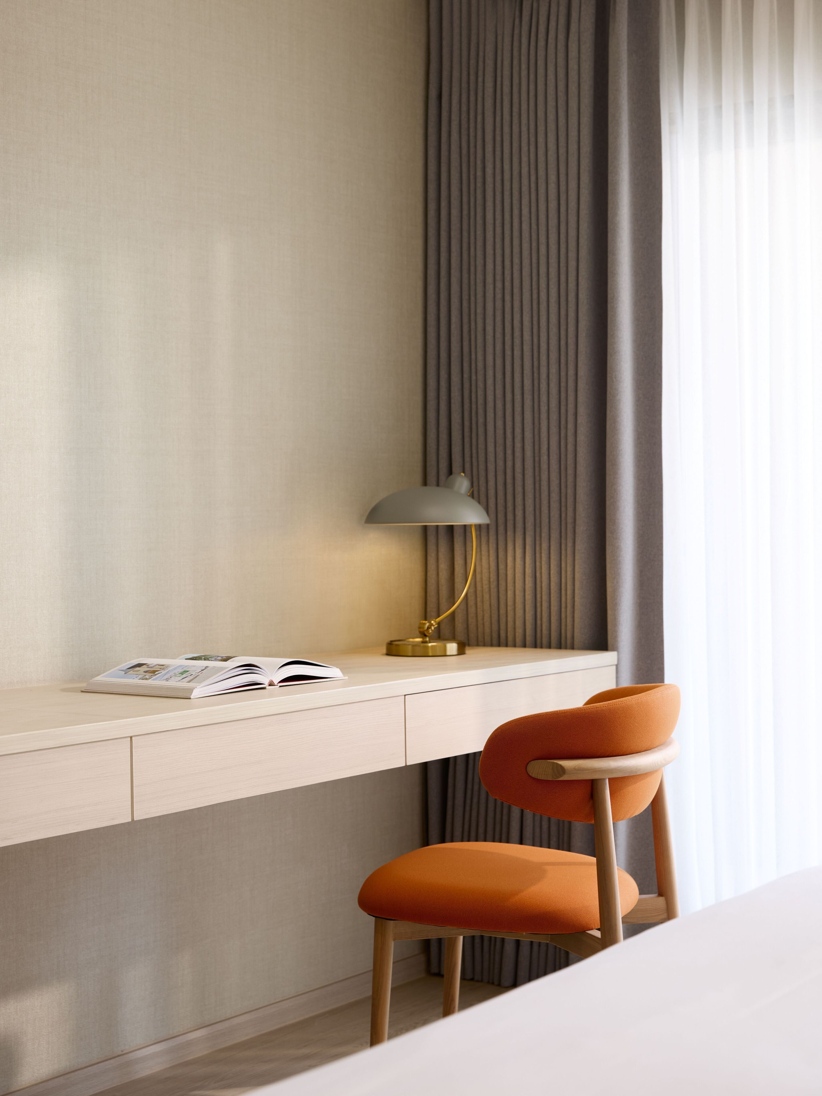 A modern hotel room with a desk, a lamp, and an orange chair.