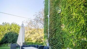 Un patio al aire libre con una mesa, sillas, una sombrilla y una pared cubierta de hiedra.