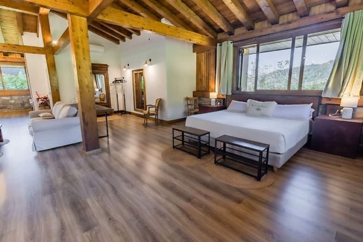 Um quarto espaçoso com uma cama grande, duas cadeiras, uma mesinha e um sofá.