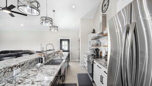 A modern kitchen with a marble countertop, stainless steel appliances, and pendant lighting. - The Wolves Den @ Frio River Vacation Rentals (Concan)