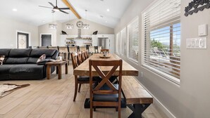 A spacious living area with a dining table, wooden chairs, a black leather sofa, and a ceiling fan. - The Wolves Den @ Frio River Vacation Rentals (Concan)