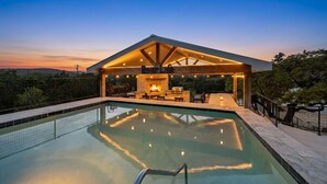 A modern outdoor pool area with a covered seating area and a fireplace. - The Wolves Den @ Frio River Vacation Rentals (Concan)