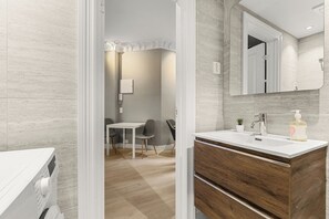 Un baño moderno con tocador de madera, un espejo y un lavabo. En la habitación contigua hay una pequeña mesa y sillas.