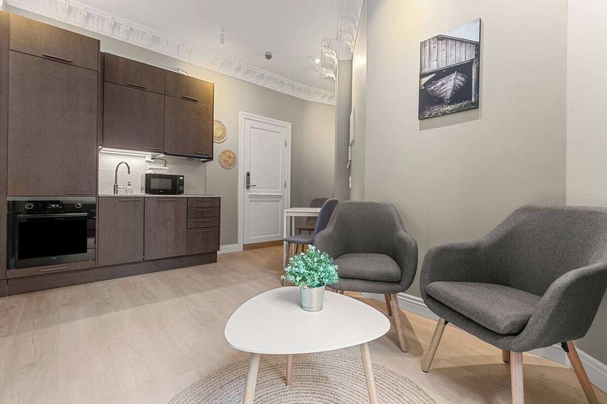 Une cuisine moderne avec des meubles en bois foncé, un plan de travail blanc et un four encastré. On y trouve une table à manger blanche avec deux chaises et une petite plante en pot.