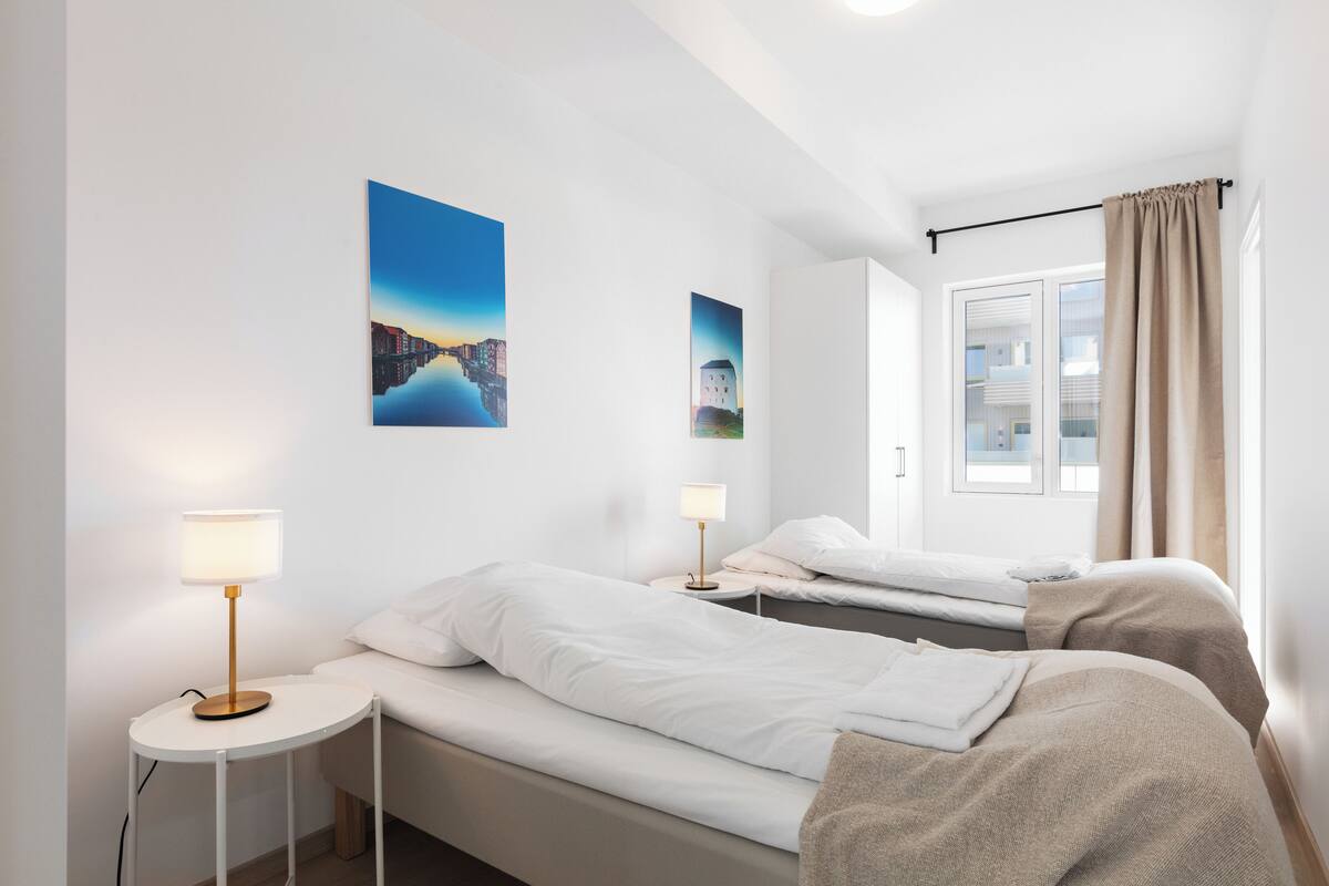 Une chambre d’hôtel avec deux lits, une petite table ronde avec une lampe, et deux tableaux accrochés au mur.