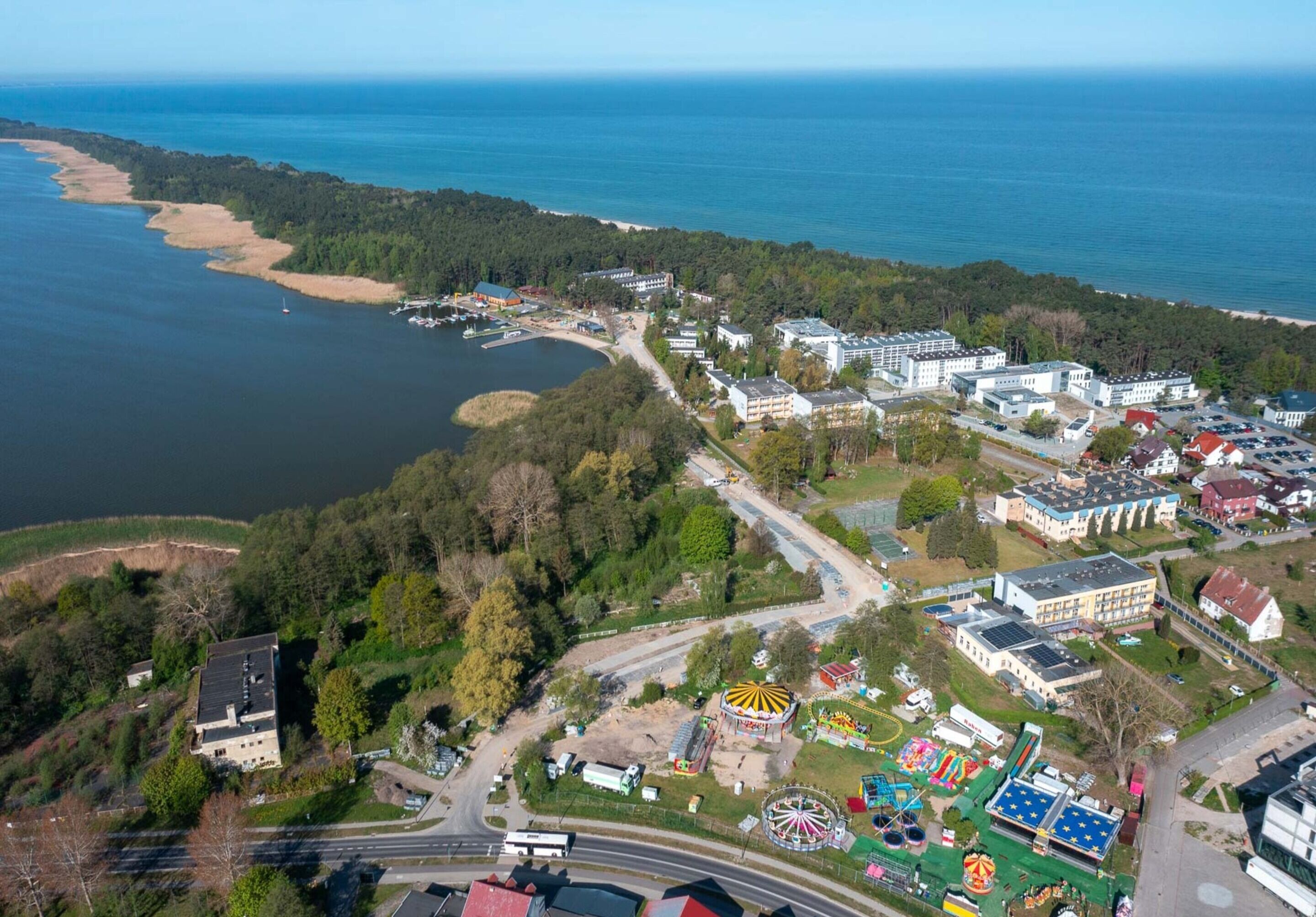 An aerial view of a coastal area with a beach, a lake, and a park with amusement rides.
