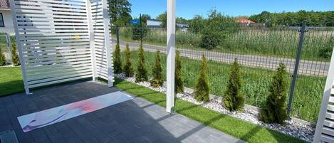 Un espacio exterior cubierto con una estructura de pérgola, un patio empedrado y vistas a una carretera y vegetación.