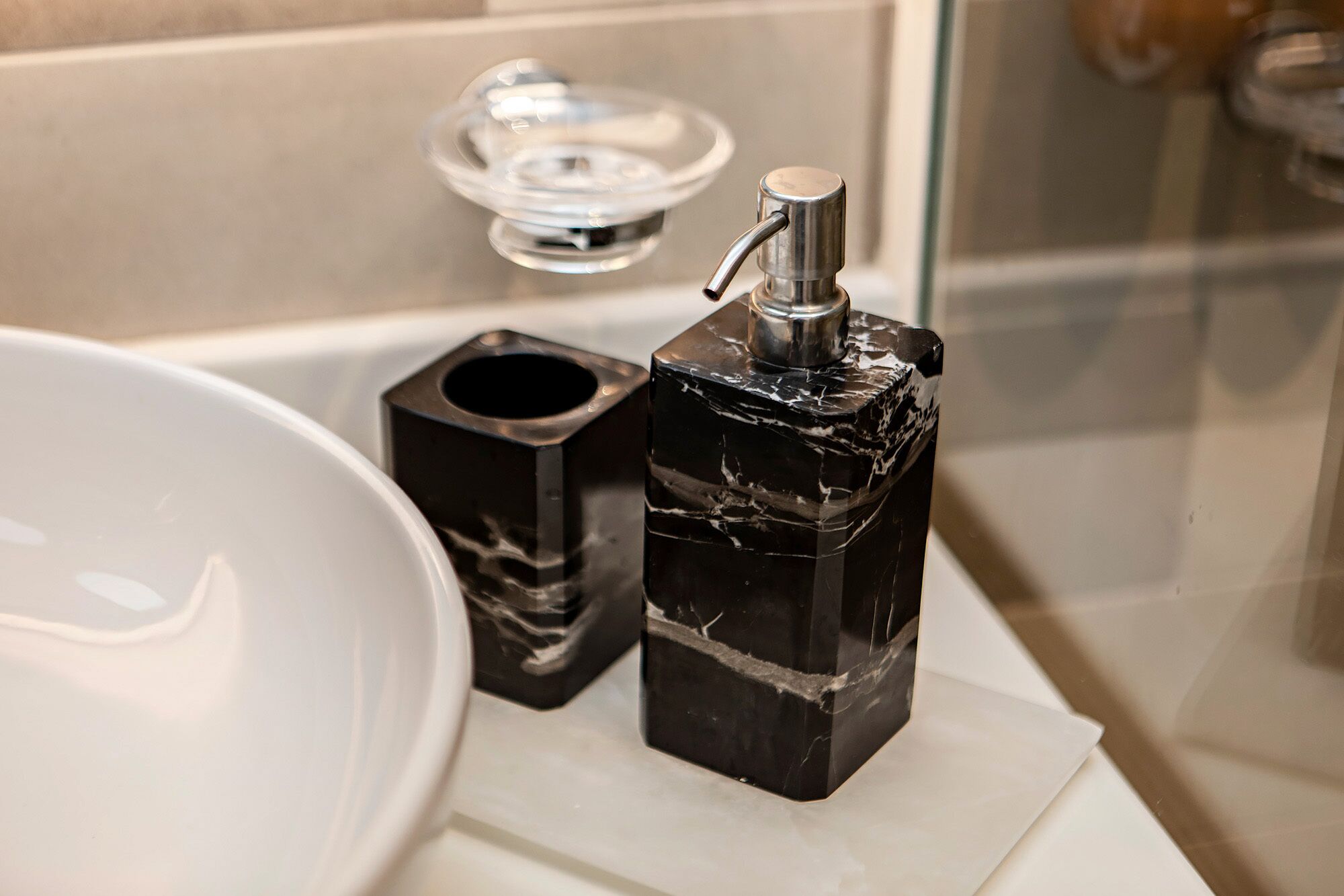 A bathroom with a white sink, a black marble soap dispenser, and a glass soap dish.