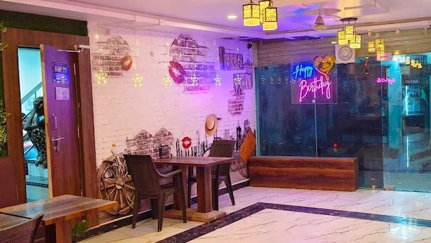 A restaurant with a rustic interior, featuring a wooden table and chairs, a neon sign, and a brick wall.