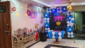 A room with a brick wall, a neon 'Happy Birthday' sign, and a blue and white balloon arrangement.