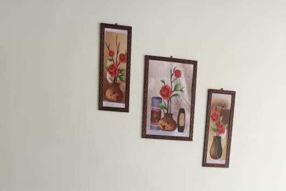 Un lit bien fait, avec du linge de lit blanc et deux oreillers, une tête de lit en bois et trois tableaux représentant des motifs floraux, encadrés et accrochés au mur au-dessus.