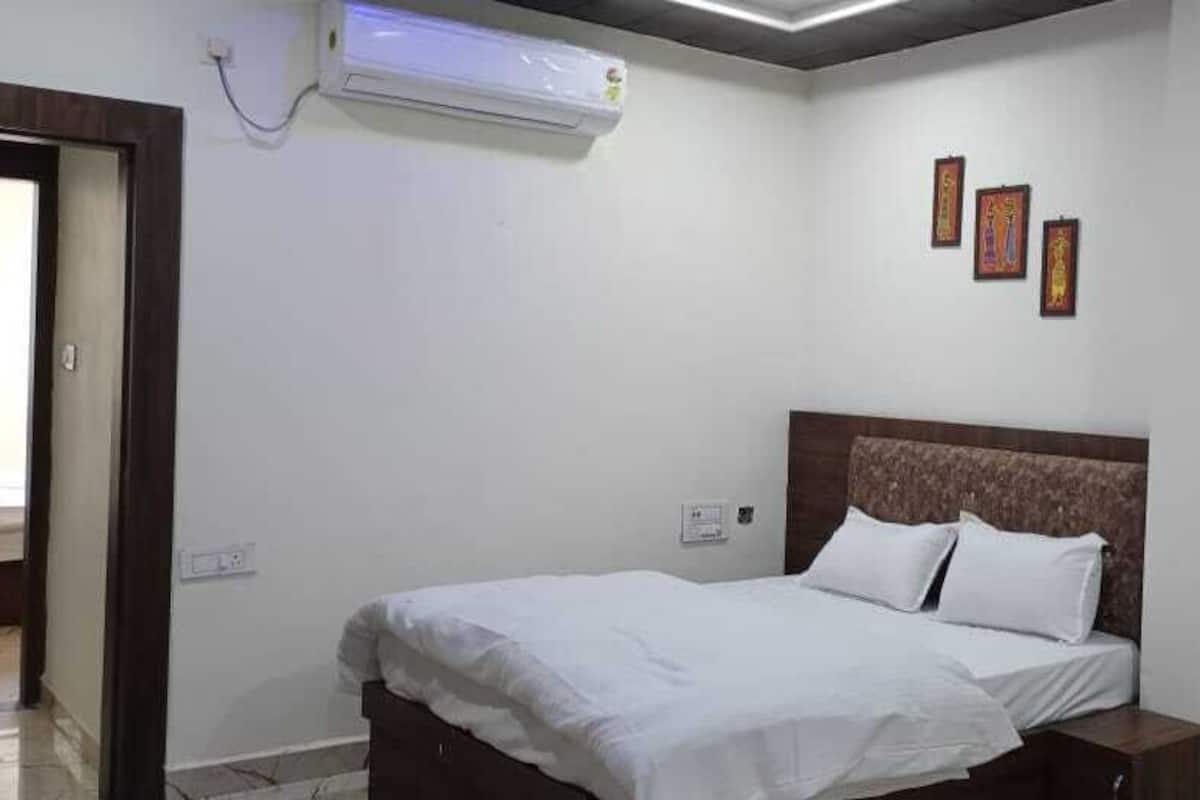 Une chambre à coucher comprenant un lit, des tables de chevet, un climatiseur fixé au mur et trois tableaux encadrés accrochés au mur.