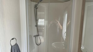 A shower enclosure with a handheld showerhead, a towel rack with a towel, and a bottle of blue liquid soap on the sink. - Caravanbreak/ 3bed/ Petsok/freep/ Tv/ Wifi (Launceston)