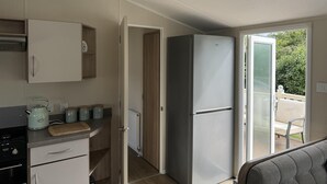 A compact kitchen with a refrigerator, a stove, and a small countertop with a cutting board and jars. - Caravanbreak/ 3bed/ Petsok/freep/ Tv/ Wifi (Launceston)