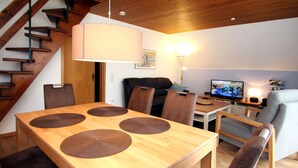 Ein modernes Wohnzimmer mit einem Holzesstisch, bequemen braunen Sesseln, einer Couch, einem Fernseher und einer Treppe.