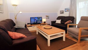 Ein modernes Wohnzimmer mit einem braunen Sofa, einem Holztisch und einem Fernseher auf einem Schrank.
