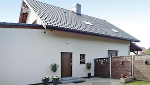 Ett modernt hus med ett sluttande tak, en trädörr och ett litet fönster. Det finns krukväxter och ett trästaket på gården.