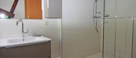 A bathroom with a glass-enclosed shower, a sink with a mirror above it, and a cabinet below.