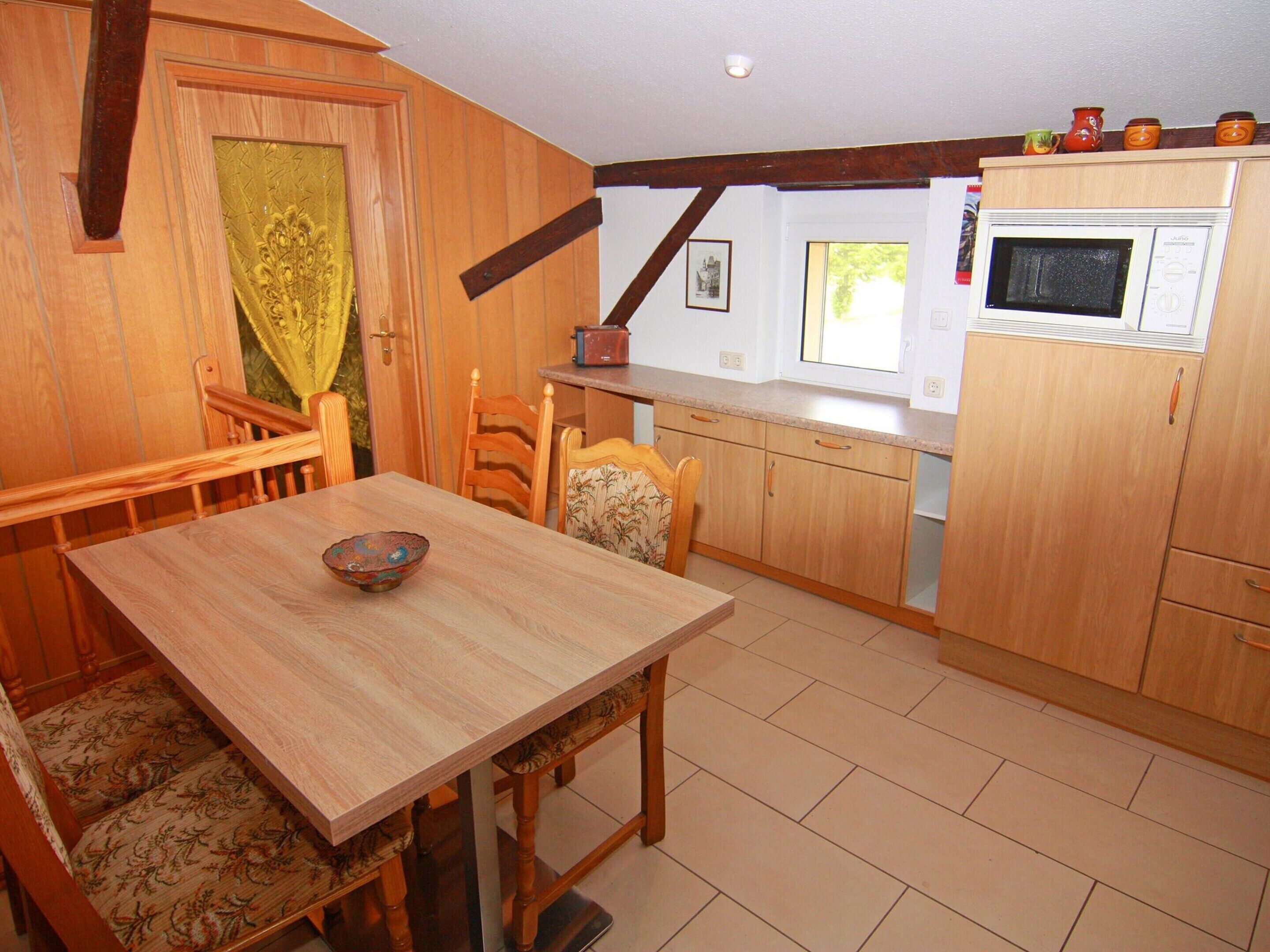 A kitchen with wooden cabinets, a dining table, chairs, a microwave, and a window with natural light.