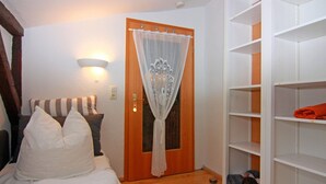 A bedroom with a bed, a nightstand, a lamp, a wardrobe, and a door with a curtain. - Behagliche Ferienwohnung im Idyllischen Korchow (Biendorf)