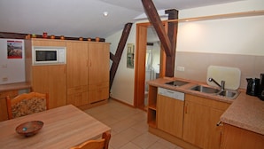 A compact kitchen with wooden cabinets, a microwave, a sink, and a dining table with chairs. - Behagliche Ferienwohnung im Idyllischen Korchow (Biendorf)