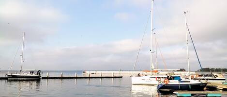 A marina with several sailboats docked, calm water, and a clear sky.