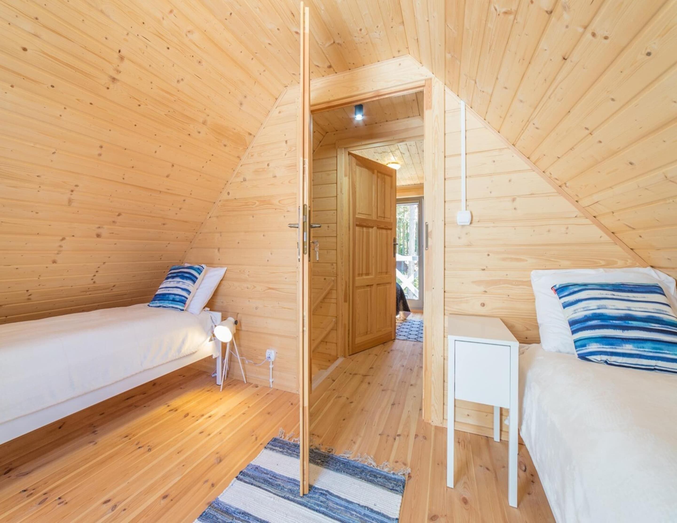 A cozy attic bedroom with two beds, wooden walls, and a small bedside table.