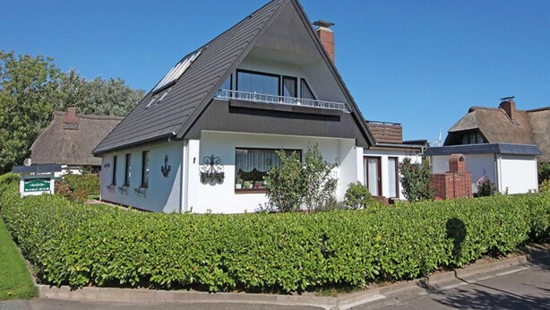 Een huis met twee verdiepingen, een schuin dak, een balkon en een bakstenen schoorsteen.