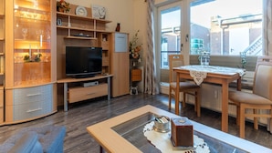 Een gezellige woonkamer met een televisie, houten kasten, een eettafel en een balkon met uitzicht.