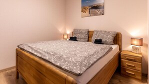 Een slaapkamer met een houten bed, beddengoed met een patroon, twee bedlampjes, een nachtkastje en een ingelijste foto aan de muur.