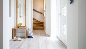 Un couloir avec un escalier en bois, un miroir, un banc sur lequel est posé un sac à rayures, et une paire de chaussures sur le sol.