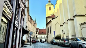 A cobblestone street with historic buildings, a church, and parked cars. - Apartments by Jacob (Prague)