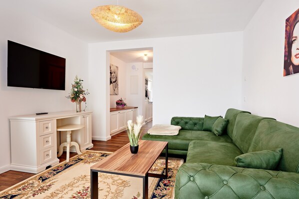 A modern living room with a green sofa, a wooden coffee table, and a flat-screen TV mounted on the wall. - Luxusappartement Sissi in Wendorf im Bernsteinland (Kuhlen-Wendorf)