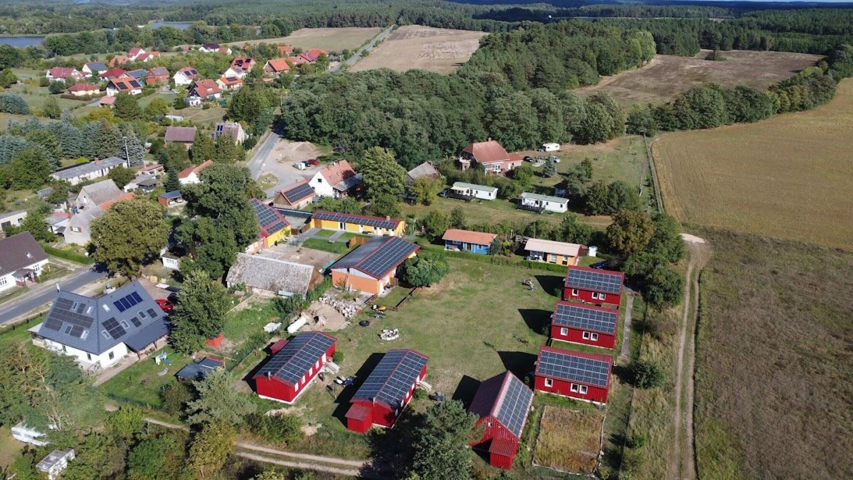Eine Vogelperspektive auf eine ländliche Gegend mit Häusern, von denen einige mit Solaranlagen ausgestattet sind, umgeben von Feldern und Wäldern.