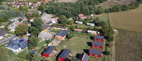 An aerial view of a rural area with houses, some with solar panels, surrounded by fields and forests.