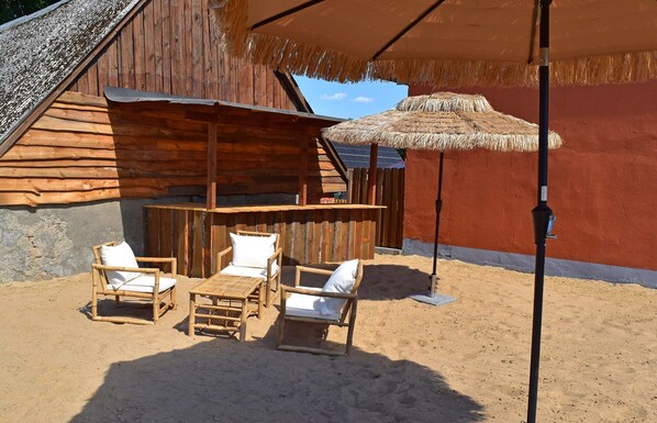 A wooden cabin with a thatched roof and a sandy floor.