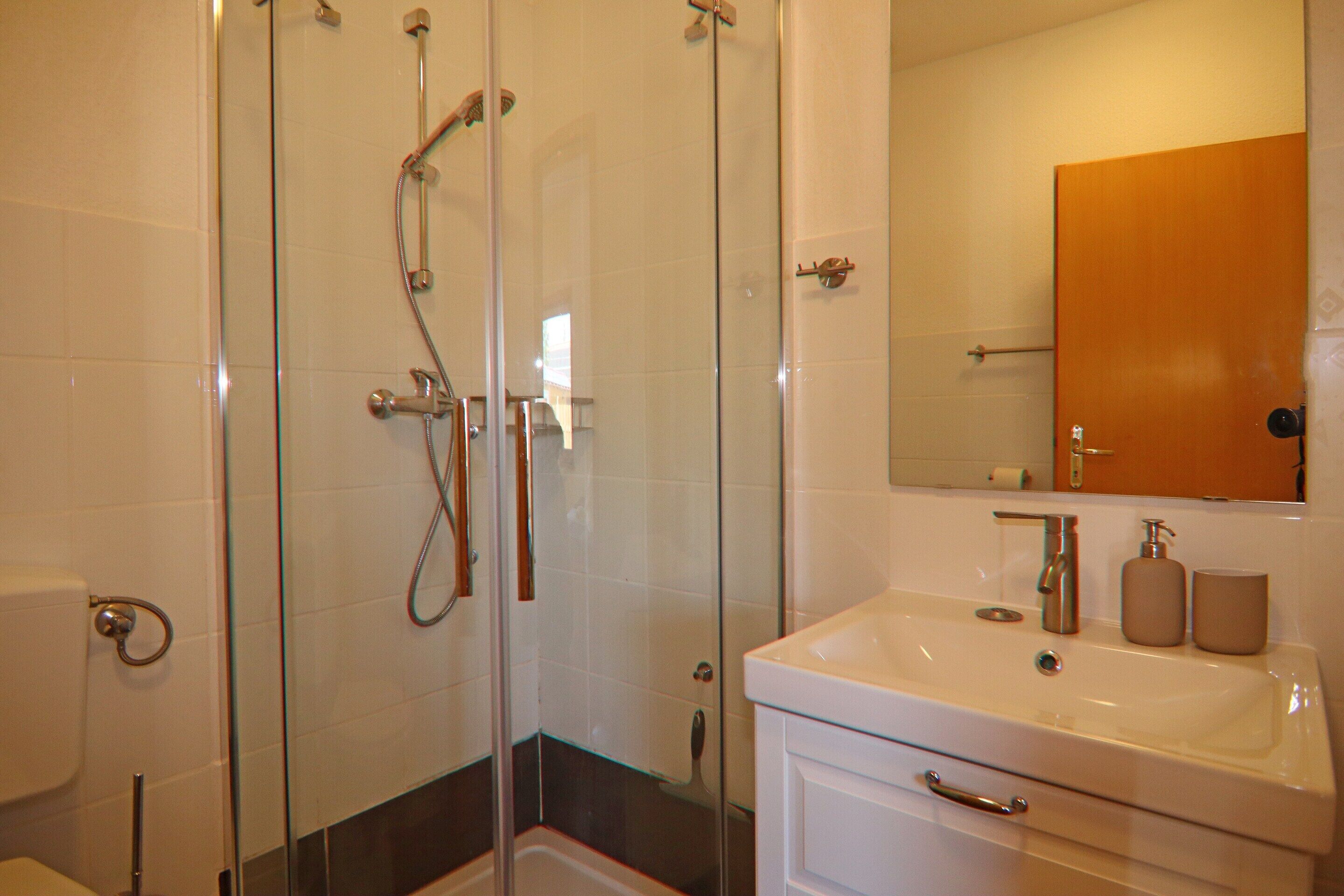 Un baño con ducha de vidrio, lavabo blanco y mueble de madera.