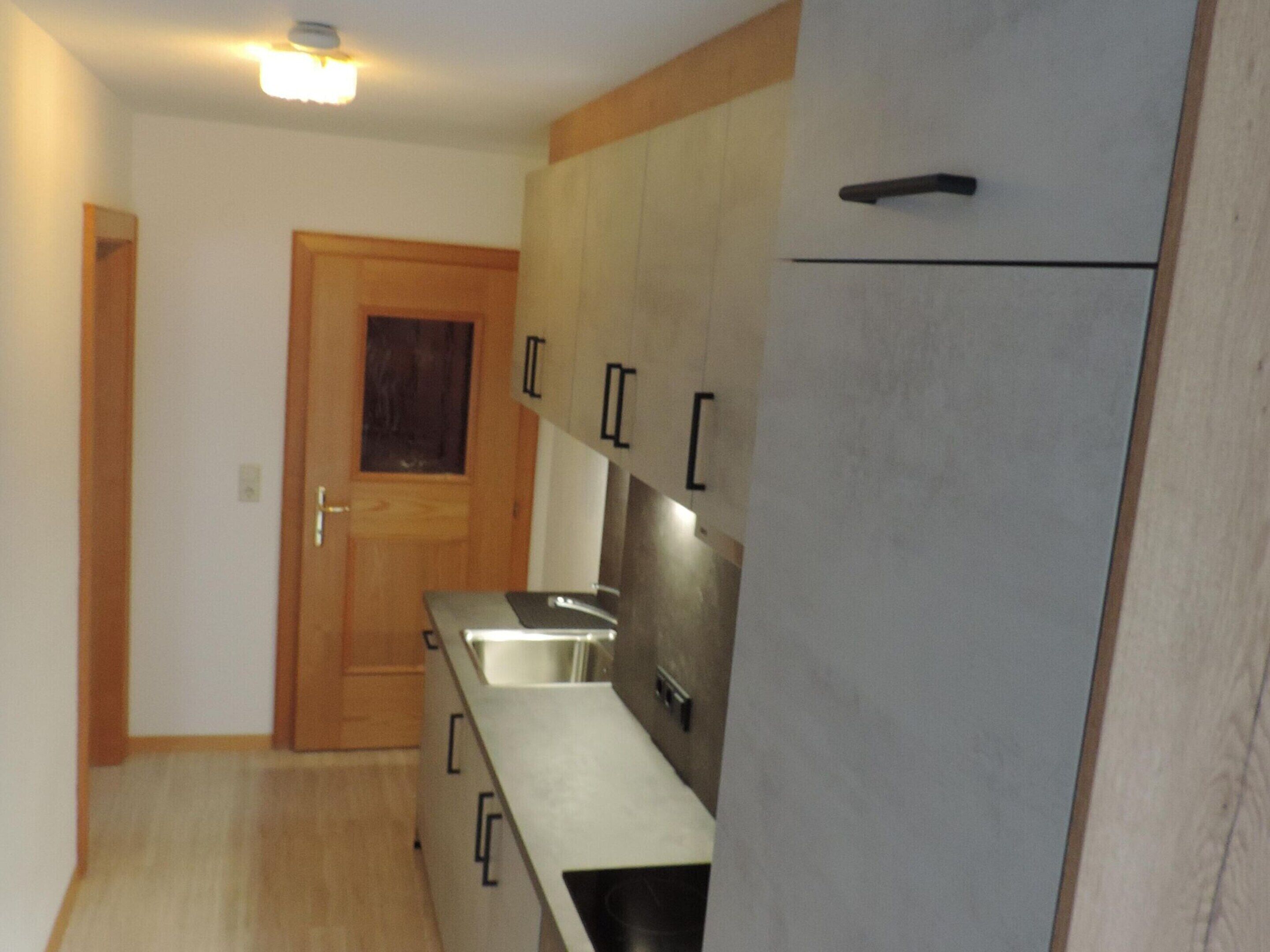 Une cuisine compacte avec des meubles en bois, un évier en acier inoxydable et un réfrigérateur encastré.
