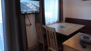 Ein Hotelzimmer mit an der Wand montiertem Fernseher, einem Esstisch mit Stühlen, einer Fernbedienung und einer dekorativen Schale auf dem Tisch.