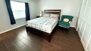 A bedroom with a bed, a chair, a nightstand, and a window with curtains. - Peaceful and Beautiful Home (Brandon)