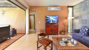 Uma sala de estar com sofá, poltronas, mesa de centro, televisão e um aparador decorativo.