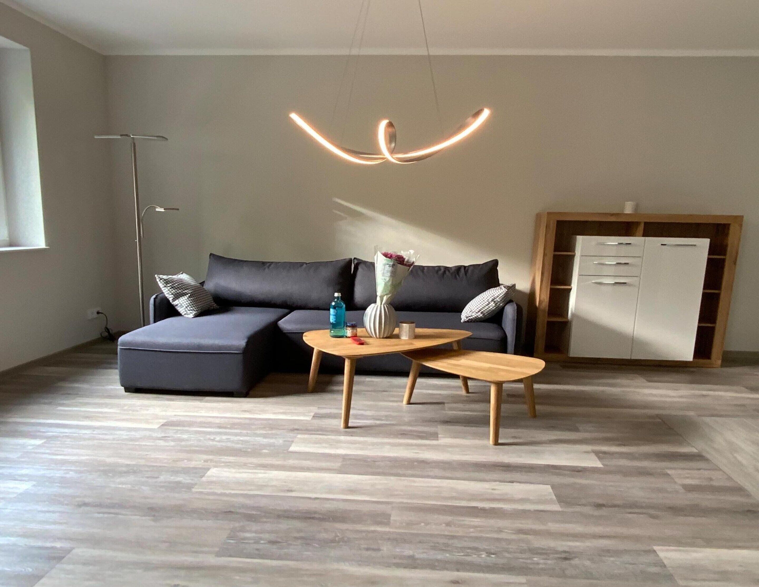 En moderne stue med en hjørnesofa, to træsideborde og en hængende lampe.