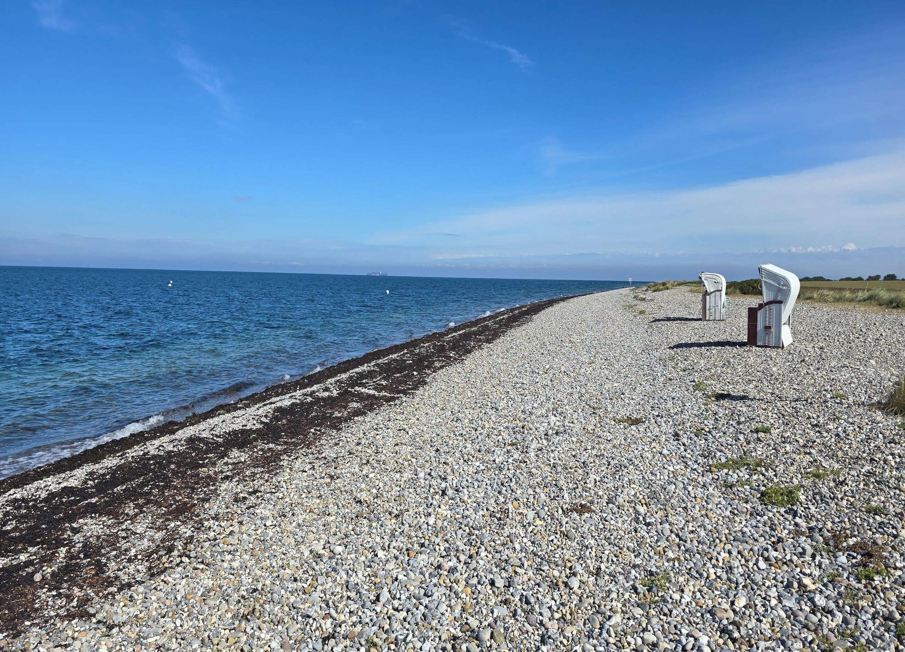 Une plage de galets avec deux chaises blanches donnant sur la mer.