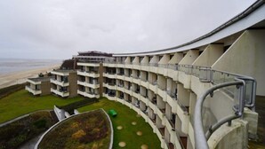 Un hotel a più piani con facciata curva, un cortile curato con giardino a forma circolare e vista sulla spiaggia.