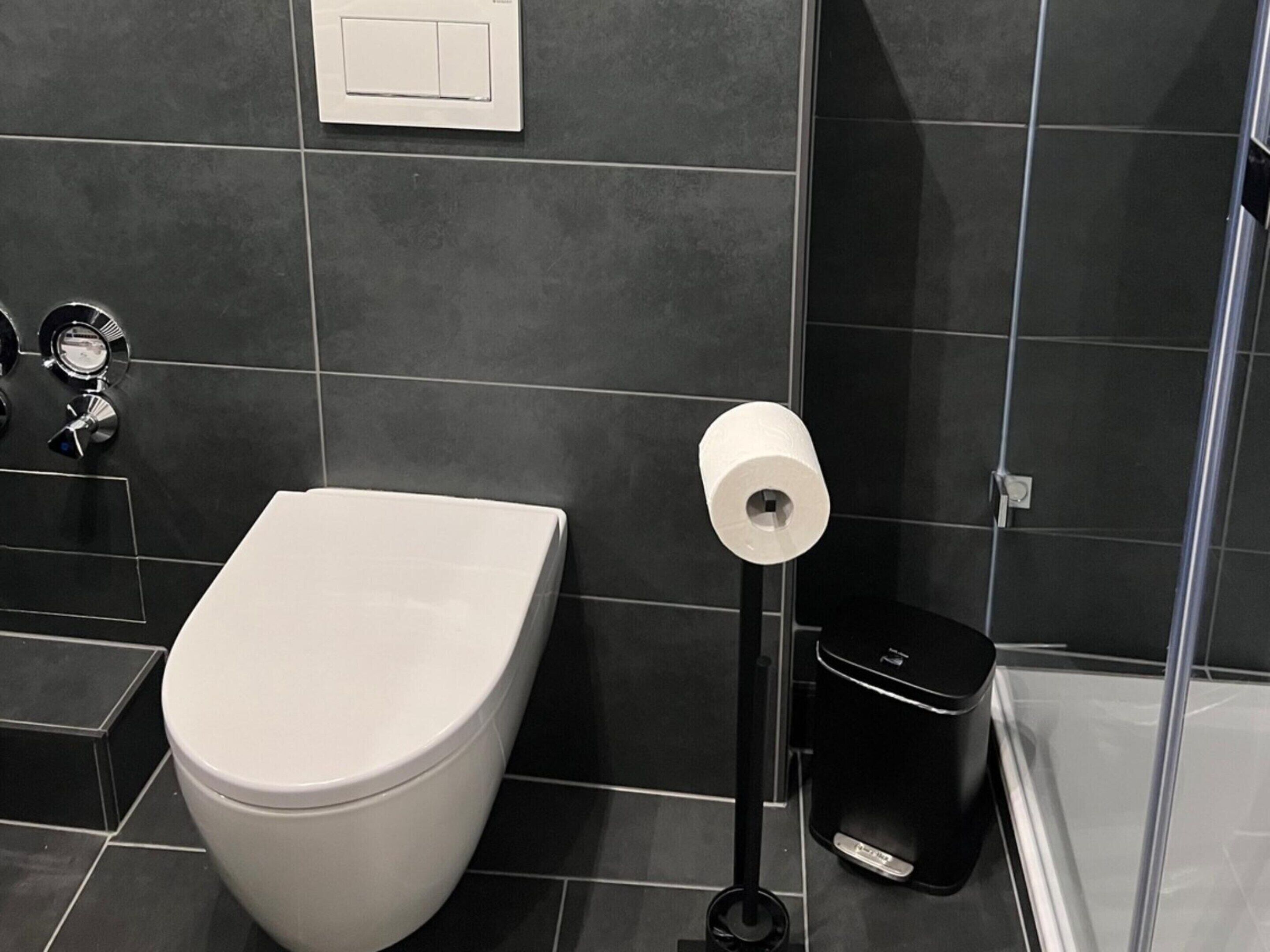A modern bathroom with a toilet, a toilet paper holder, and a trash bin.