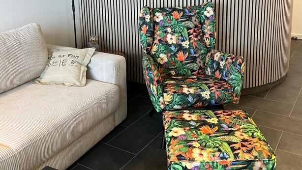 A striped sofa with a pillow, a floral-patterned armchair, and a matching ottoman in a room with a striped wall and tiled floor. - Ferienwohnung mit Meerblick in Wyk auf Foehr (Wyk auf Foehr)