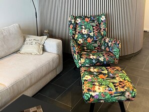 A striped sofa with a pillow, a floral-patterned armchair, and a matching ottoman in a room with a striped wall and tiled floor. - Ferienwohnung mit Meerblick in Wyk auf Foehr (Wyk auf Foehr)