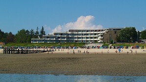 A beach with a building in the background, a pier extending into the water, and people enjoying the beach.