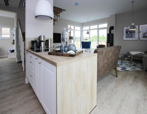A modern kitchen with a central island, white cabinetry, and a large window providing natural light. - Ferienhaus Fiete in Lancken (Dranske)